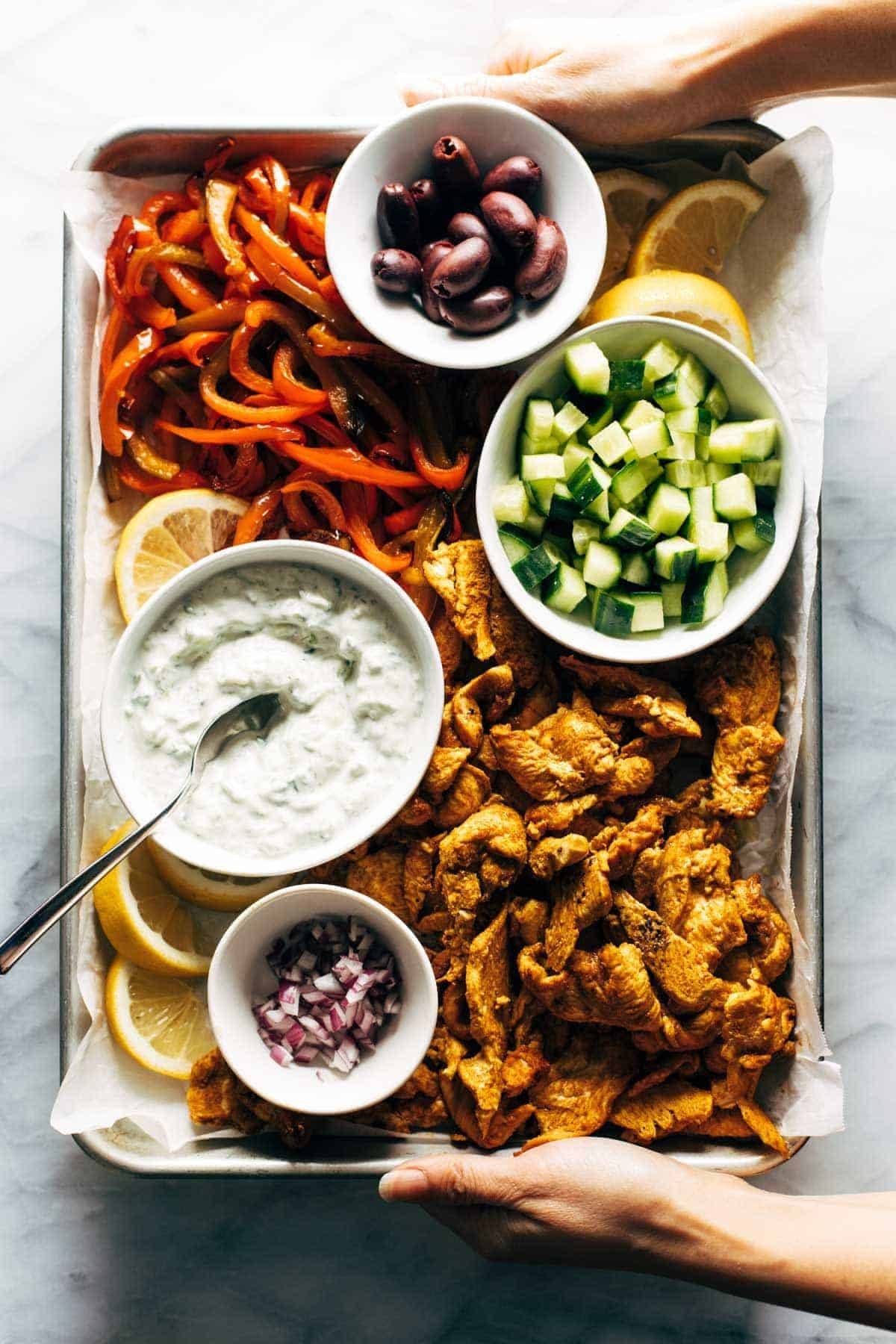 Chicken, veggies, tzatziki, and olives on a sheet pan.