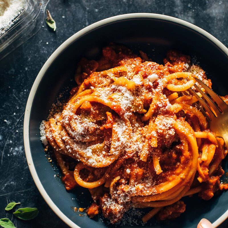 Bucatini in a bowl with red sauce and pecorino on top.