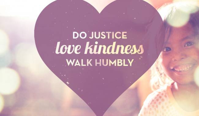 A girl smiling while standing next to a purple heart with a message of justice, love, kindness and humility.