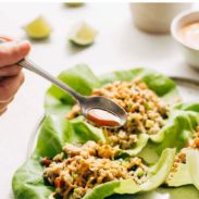 Spoon ladeling lime sauce on the chicken lettuce cups on a plate.