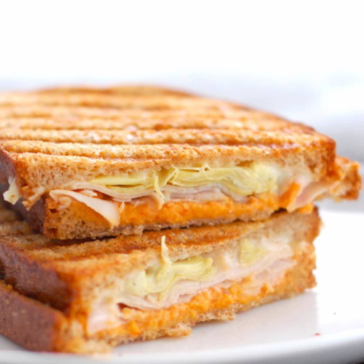 Red pepper and artichoke panini sliced in half on a white plate.